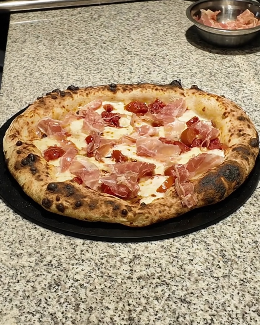 Nahaufnahme von frischen grünen Thymianblättern, die über eine gebackene Pizza gestreut werden.
