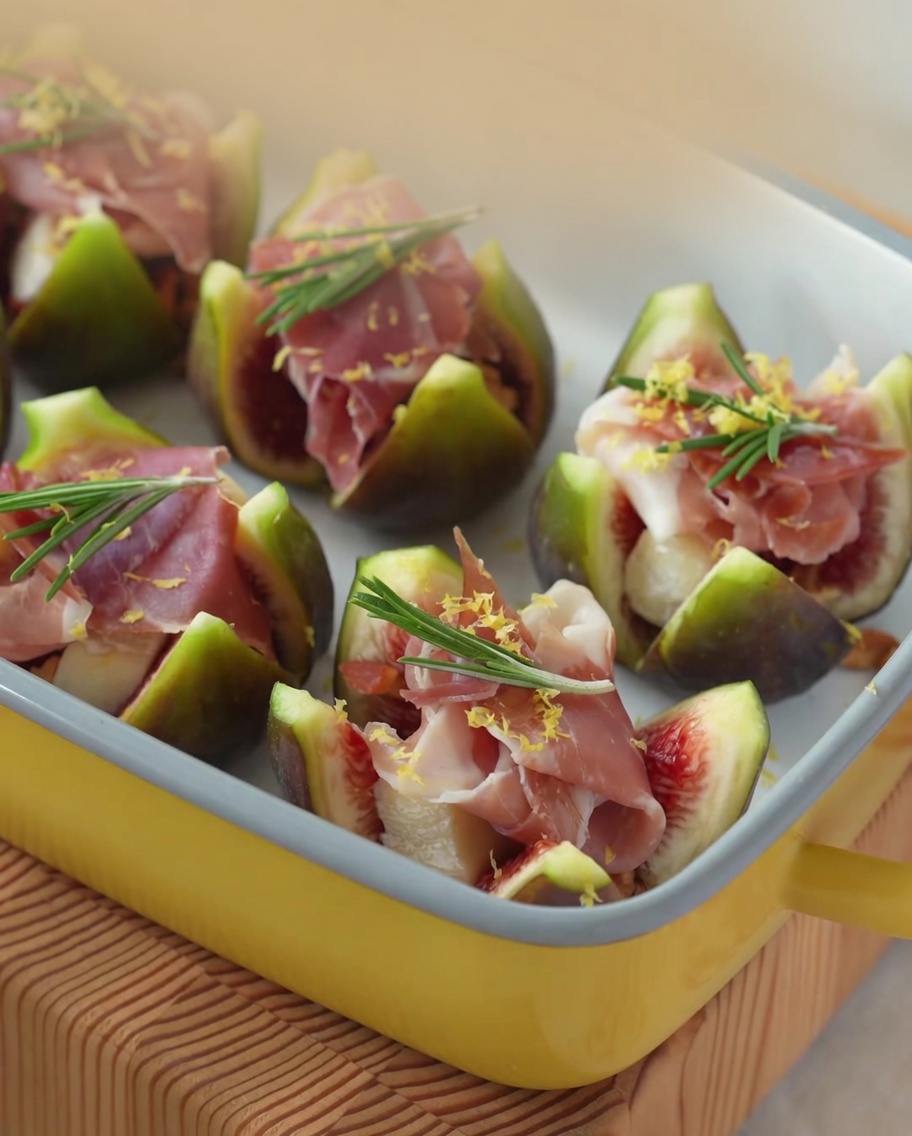 Nahaufnahme von Honig, der über mit Brie und Schinken gefüllte Feigen geträufelt wird.