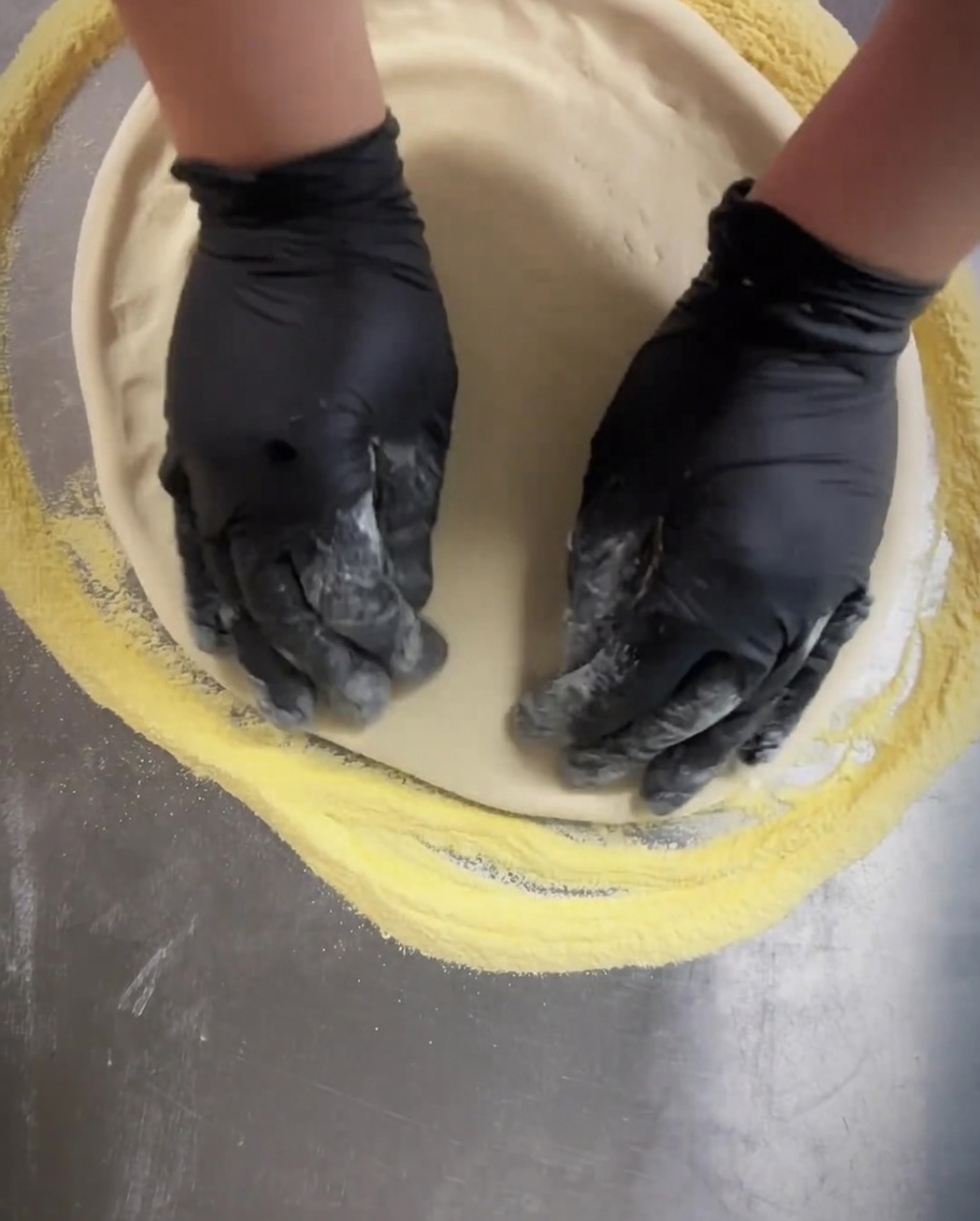 Ein Teigroller wird über den Pizzaboden gerollt, um kleine, gleichmäßige Löcher zu erzeugen.