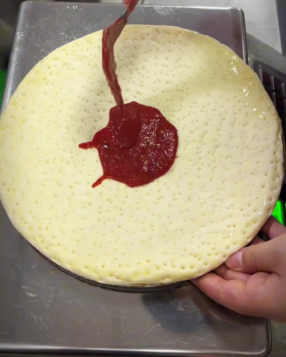 Tomatensauce wird mit der Rückseite eines Löffels auf dem Teig verteilt.