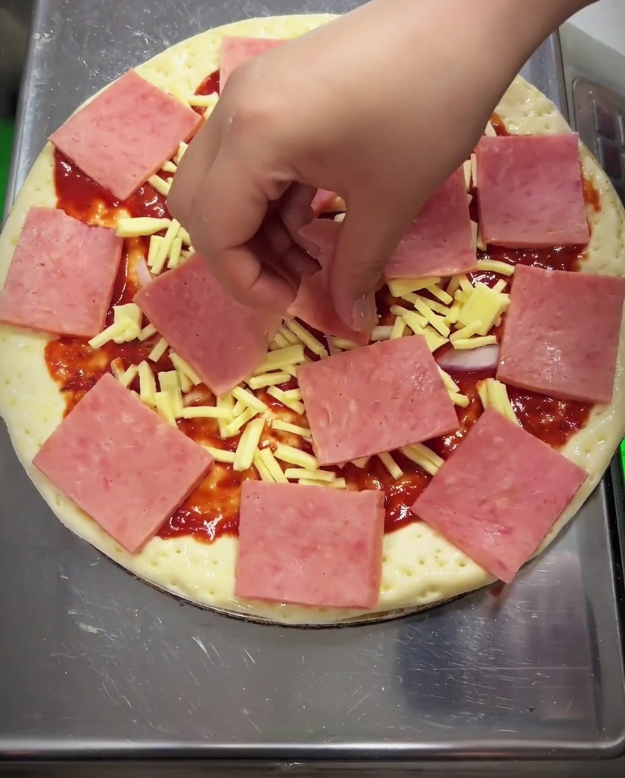 Pizza wird mit Mais, geschnittenen grünen Paprikastreifen und Champignons belegt.