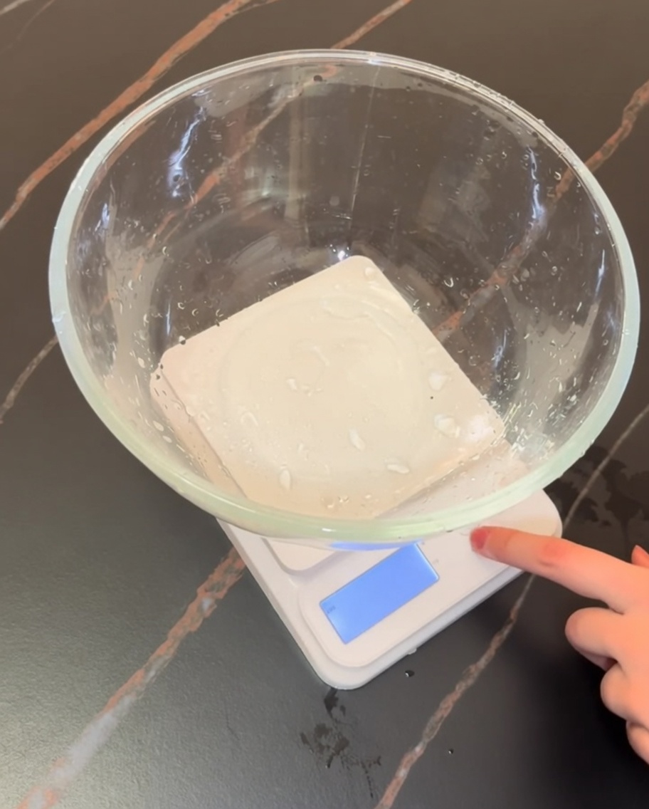 Eine digitale Küchenwaage mit einer Glasschüssel, in der Mehl und trockene Pizzazutaten abgewogen sind.