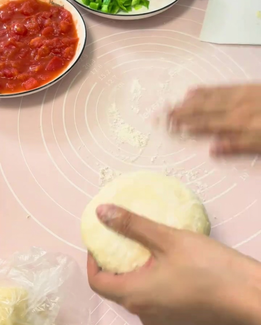 Ein Stück aufgegangener Pizzateig, der auf einer rosa Silikonbackmatte flach ausgerollt wird.