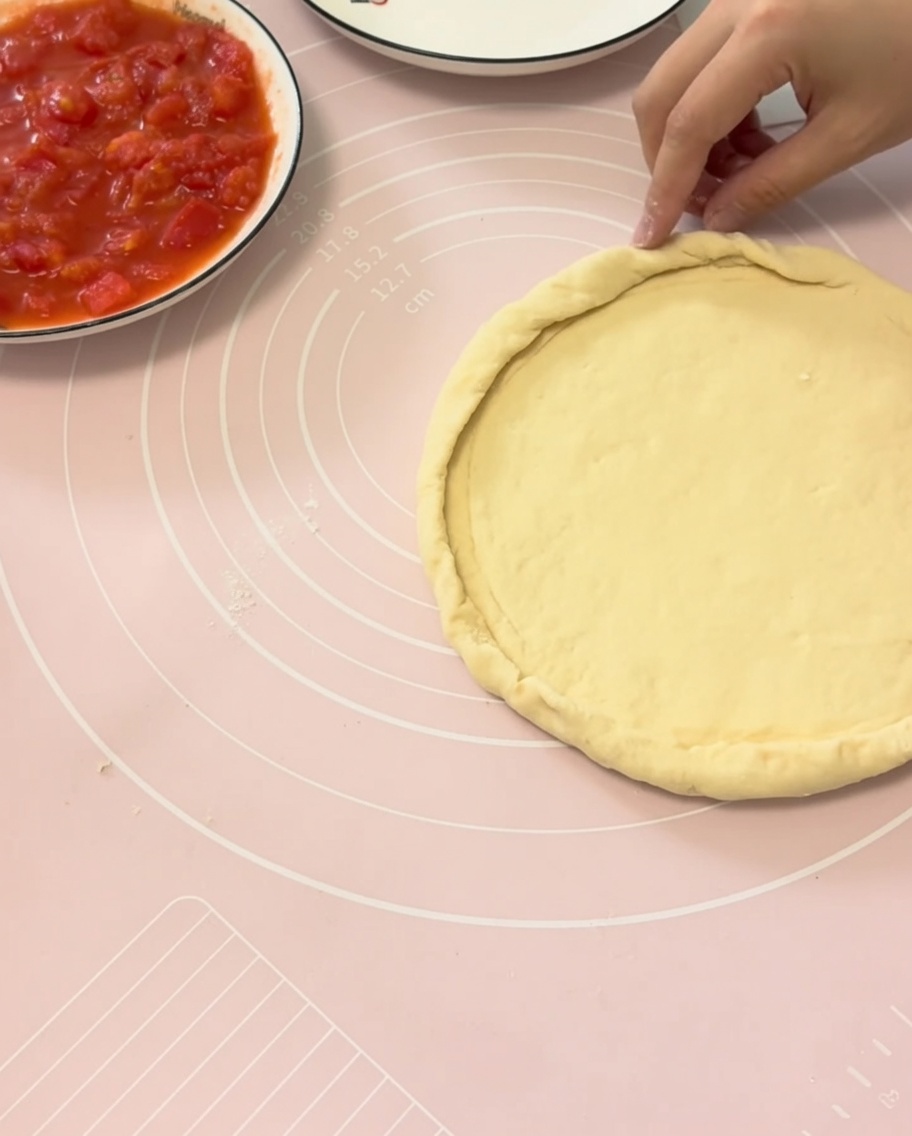 Hände falten die Ränder des Pizzateigs über einem runden Teller, um einen perfekten Rand zu formen.