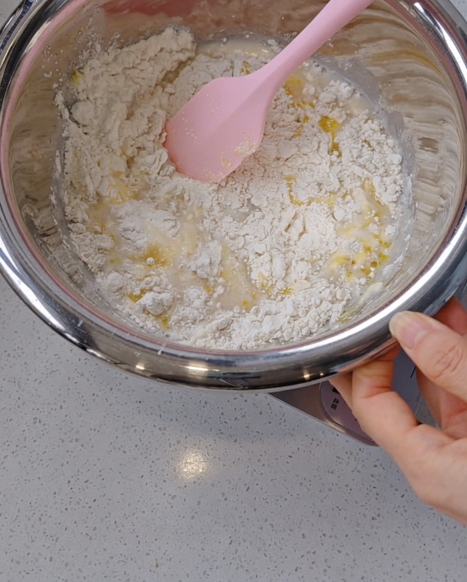 Ein Silikonspatel mischt einen zotteligen, feuchten Teig in einer Edelstahlschüssel.