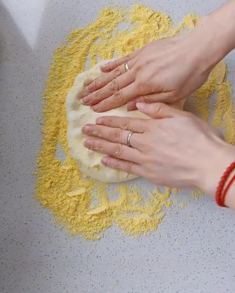Fingerspitzen drücken einen Teigfladen auf einer bemehlten Fläche flach.