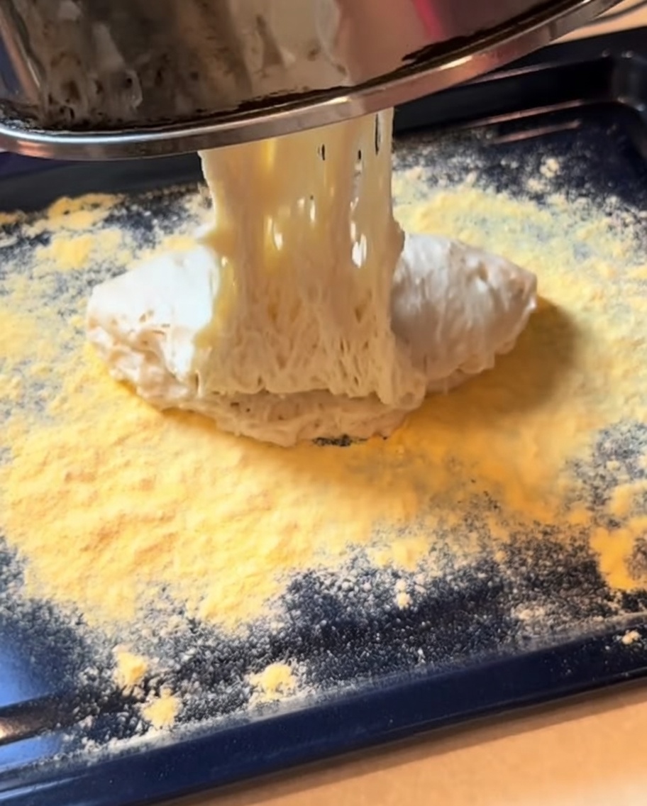 Fermentierter Pizzateig wird auf einem Backblech zu einer rechteckigen Form ausgerollt.