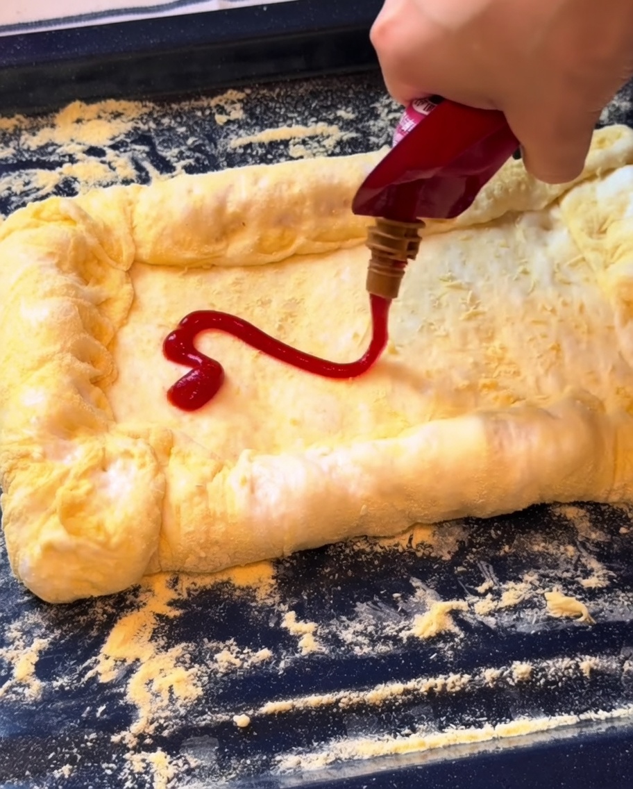 Ketchup wird auf den Boden gestrichen und mit einer Schicht geriebenem Mozzarella bedeckt.