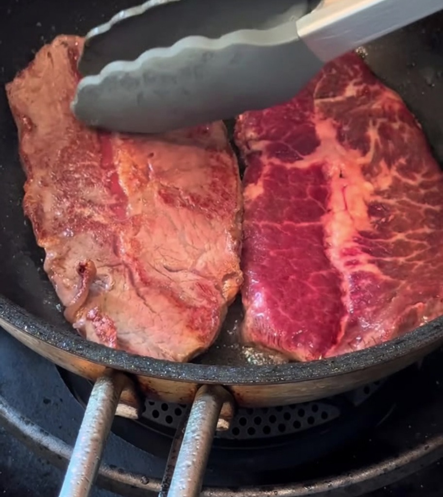 Zwei dünne Steaks braten in einer Pfanne mit einem Rosmarinzweig.