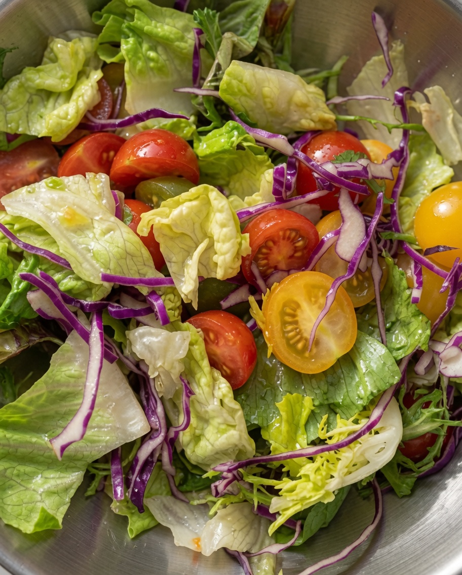 Ein bunter gemischter Salat aus grünem Blattsalat, Rotkohl und halbierten Kirschtomaten wird in einer Metallschüssel vermengt.