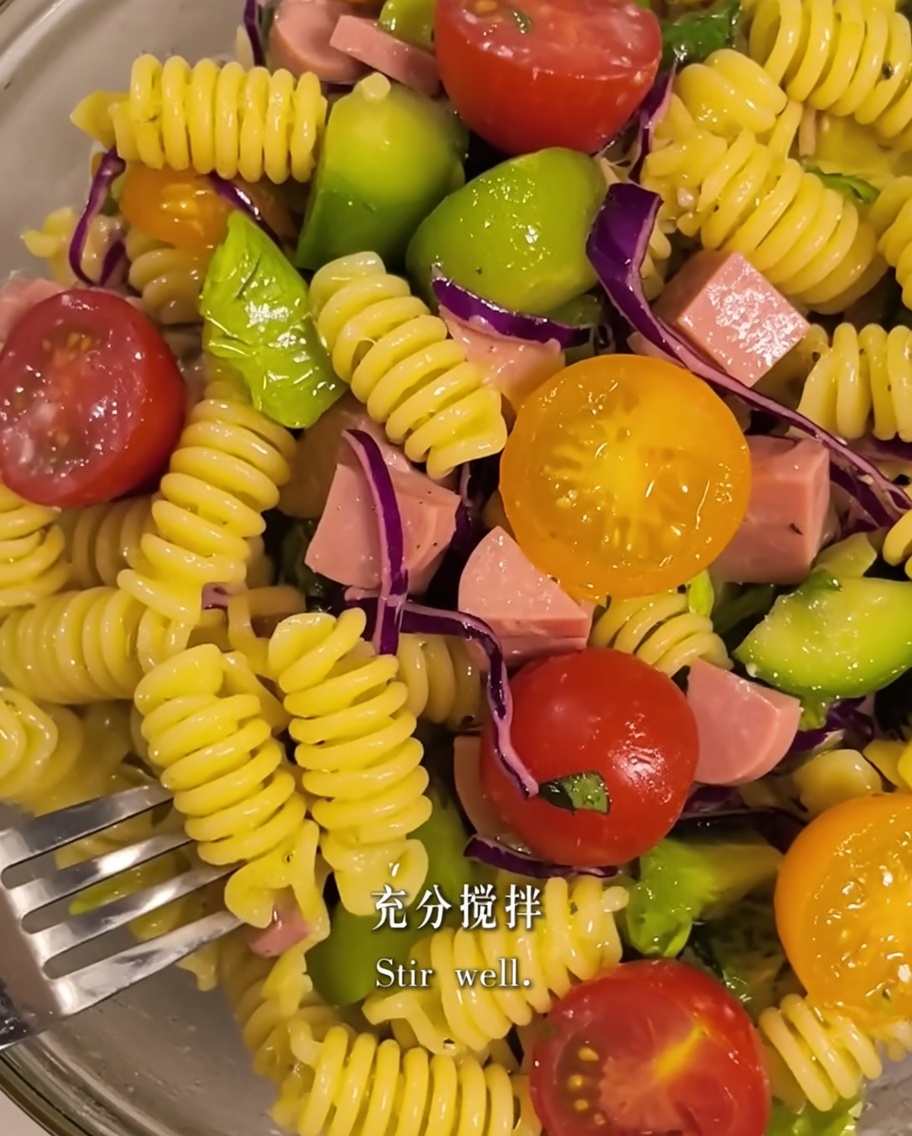 Nudeln und Salatzutaten werden in einer Schüssel mit Olivenöl vermengt.