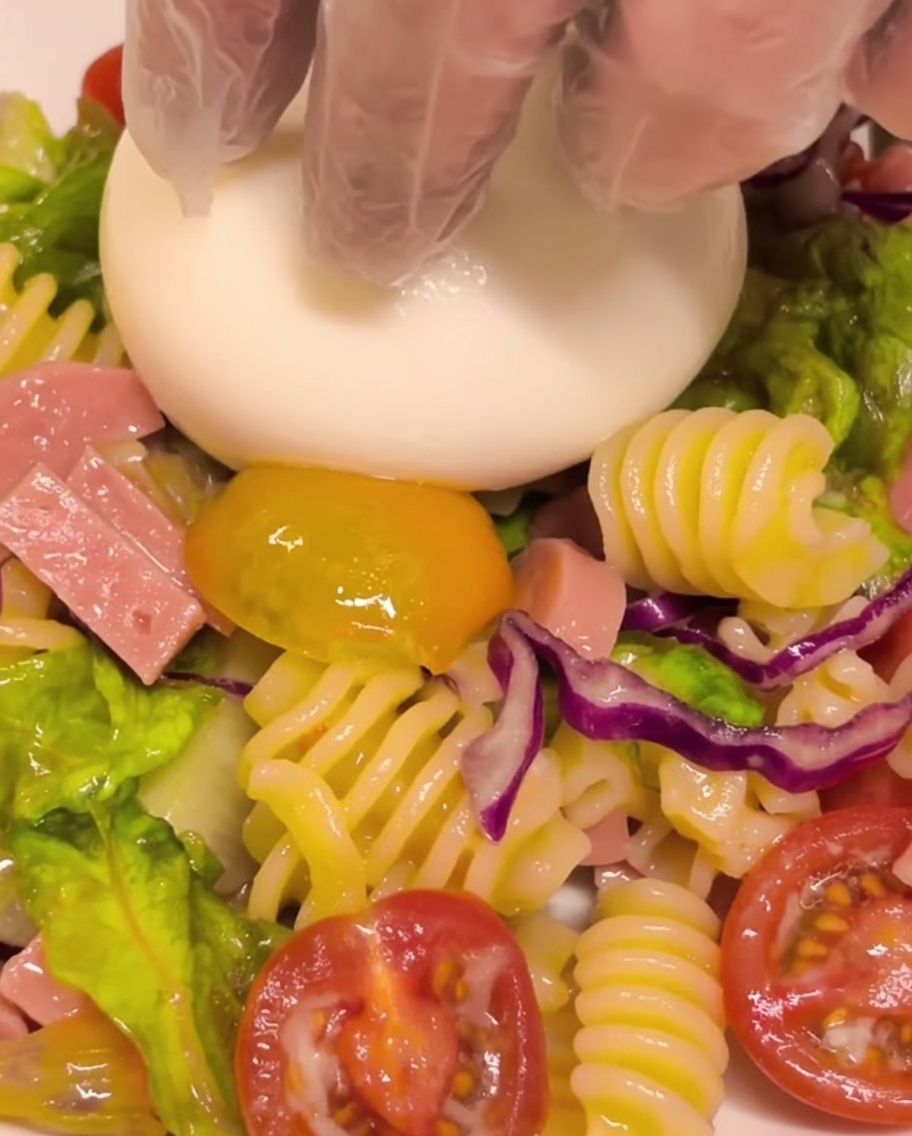 Eine frische Burrata-Kugel wird in der Mitte einer Portion des kalten Nudelsalats platziert.