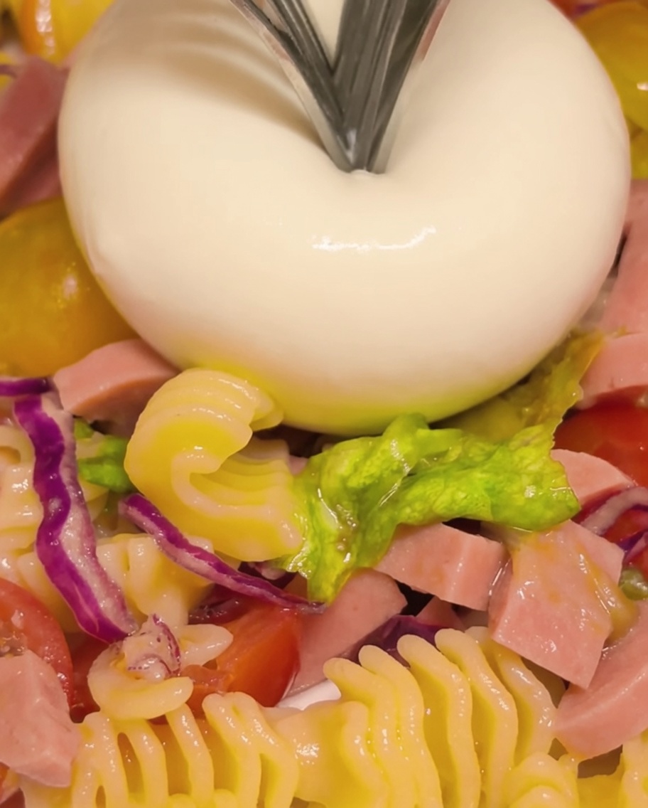 Eine Burrata-Kugel wird mit einer Gabel aufgebrochen, um den cremigen, fließenden Kern freizulegen.