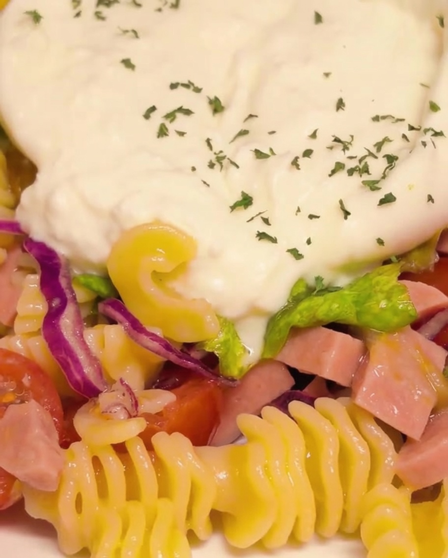 Nahaufnahme der cremigen, aufgebrochenen Burrata, die mit fein gehackter grüner Petersilie und Paprikaflocken gewürzt wird.