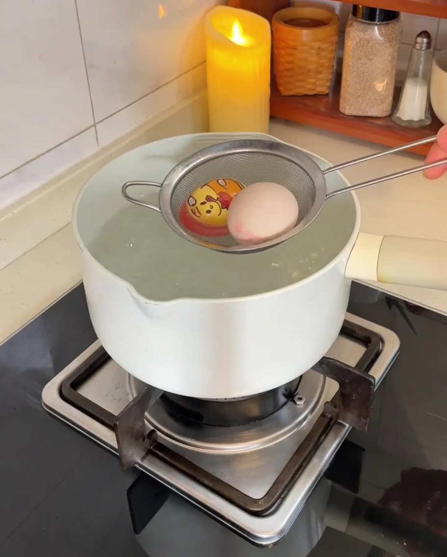 Eier werden mit einem Edelstahlsieb vorsichtig in einen Topf mit kochendem Wasser gegeben.