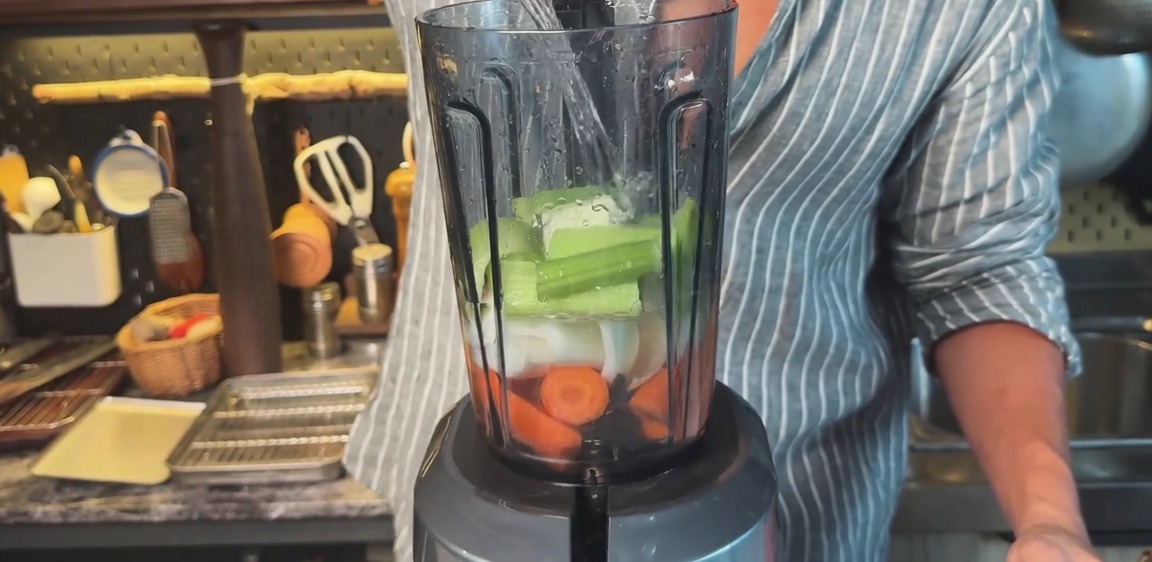 Wasser wird in einen Mixer gefüllt, der mit gehackten Karotten, Zwiebeln und Sellerie gefüllt ist.