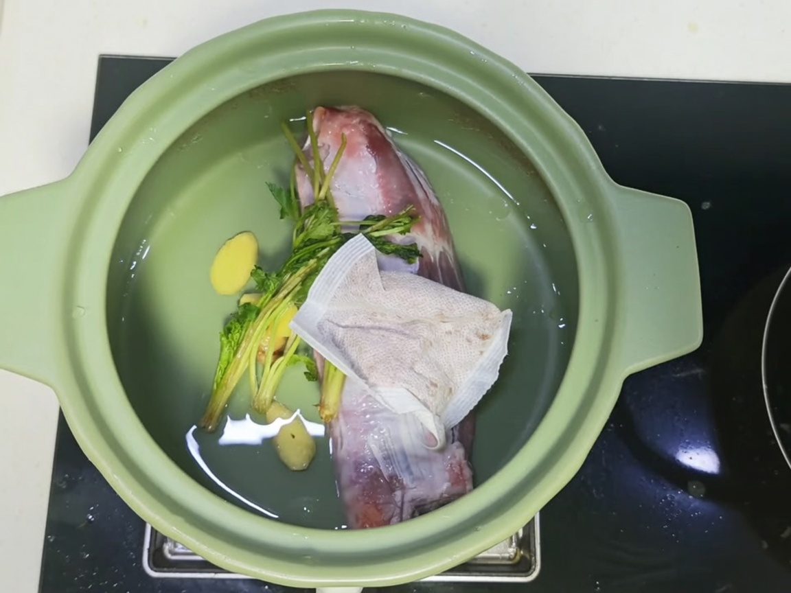 Ein Tontopf gefüllt mit Fleisch, Gewürzen und einer dunklen, herzhaften Brühenmischung.
