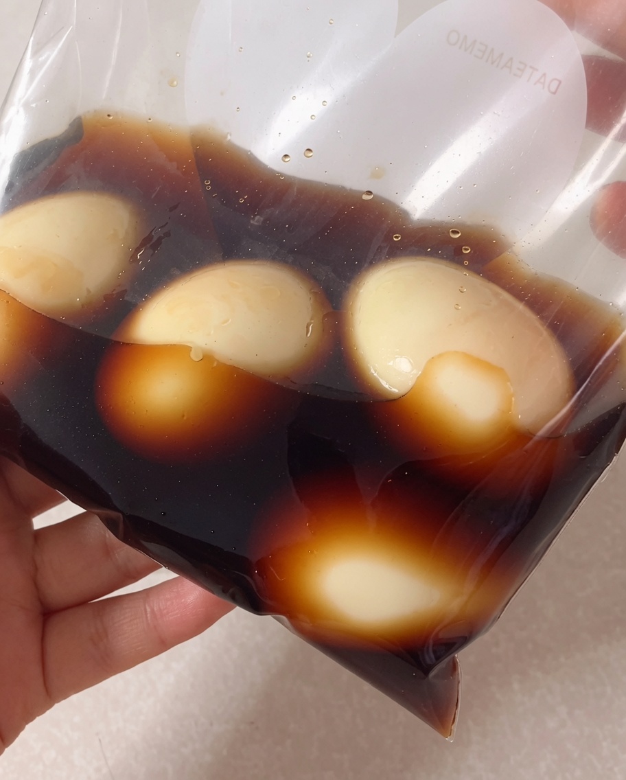 Geschälte weichgekochte Eier in einem Gefrierbeutel, die mit der dunklen Soja-Marinade übergossen werden.