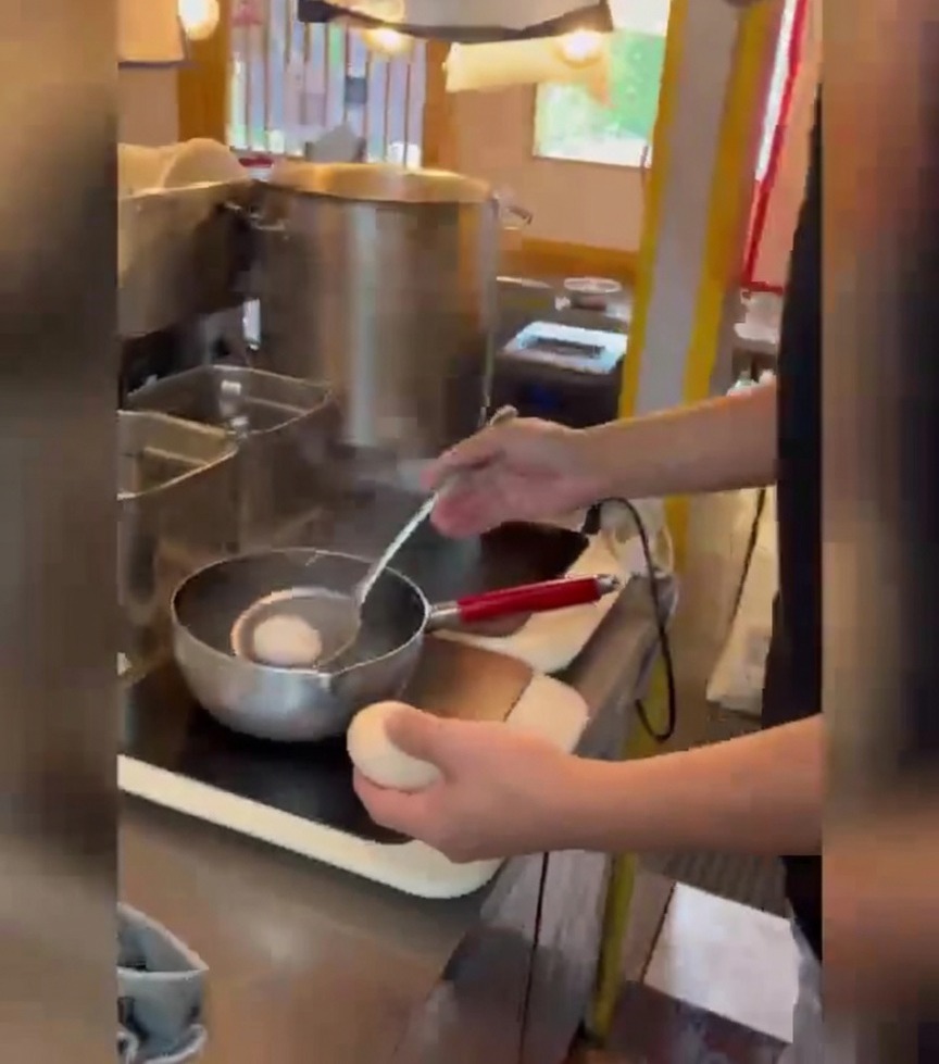 Eine Person benutzt einen Schaumlöffel, um weiße Eier vorsichtig in einen Topf mit kochendem Wasser zu geben.