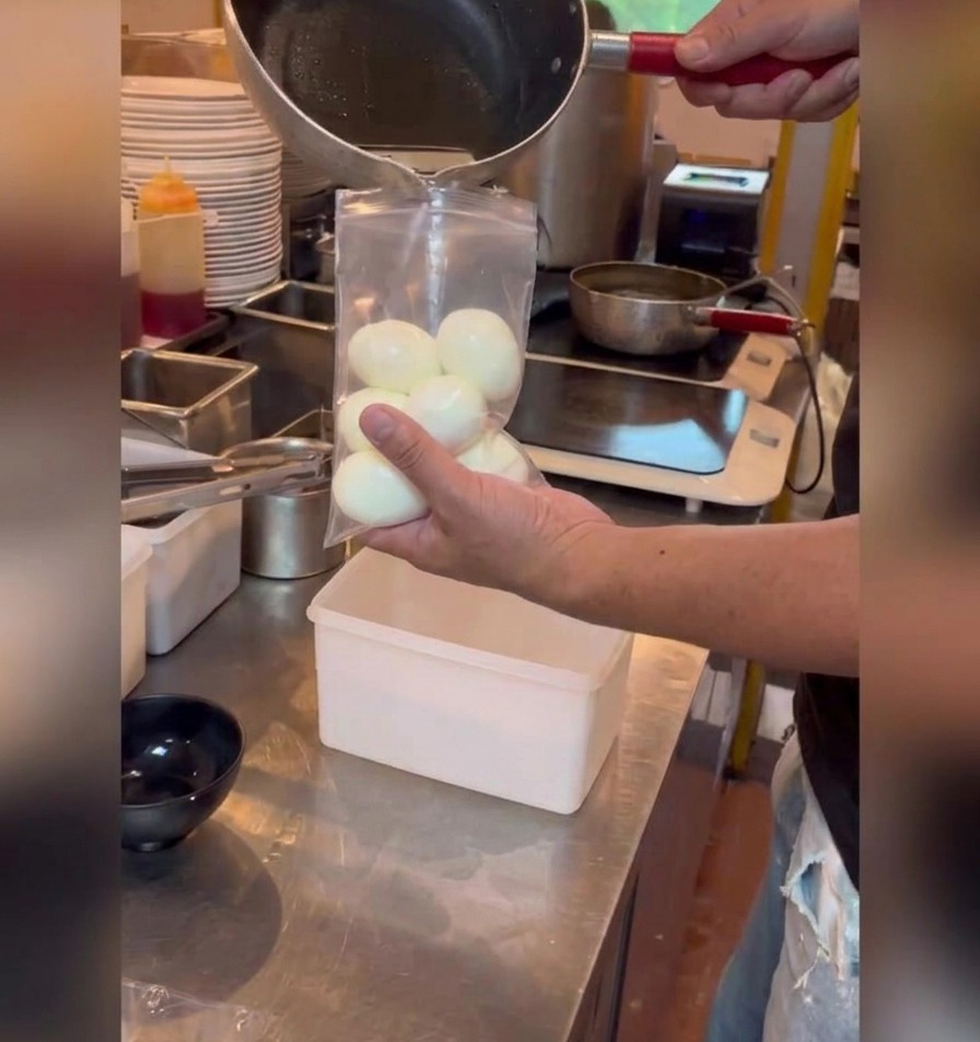 Eine dunkle Soja-Marinade wird aus einem kleinen Topf in einen Plastikbeutel mit gepellten, weichgekochten Eiern gegossen.