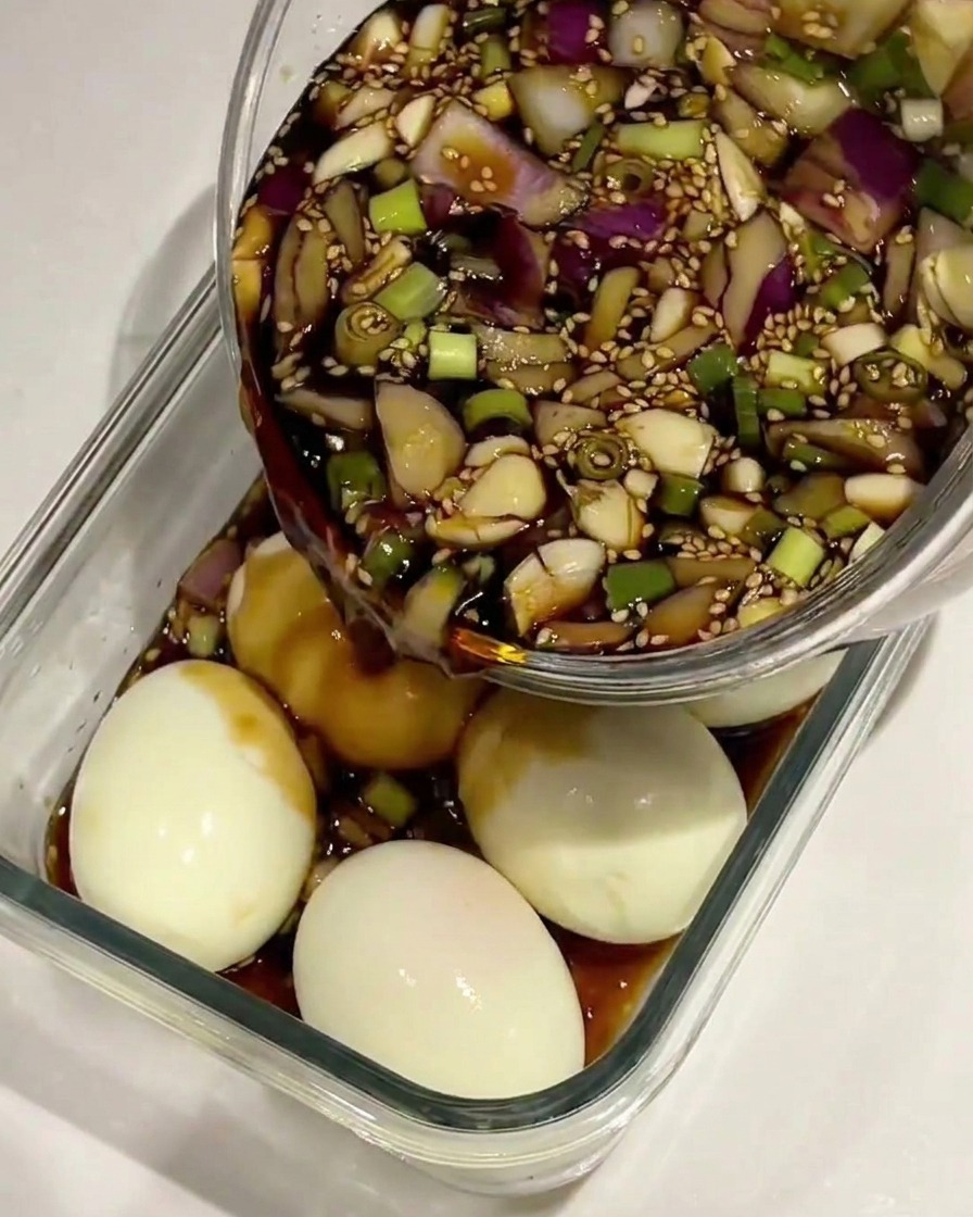 Sojasaucen-Marinade wird über gepellte, gekochte Eier in einem Glasbehälter gegossen.