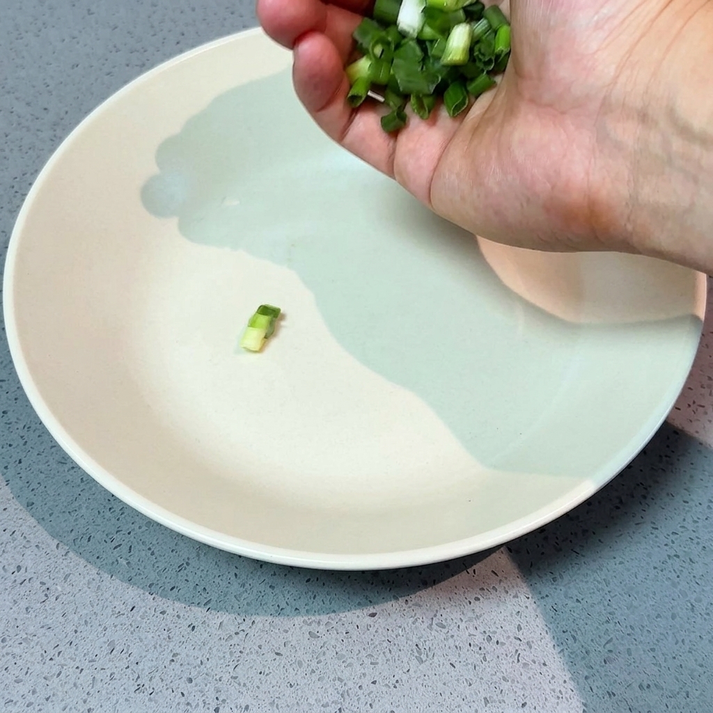 Eine Hand streut frisch gehackte Frühlingszwiebeln in eine große, flache weiße Servierschüssel.