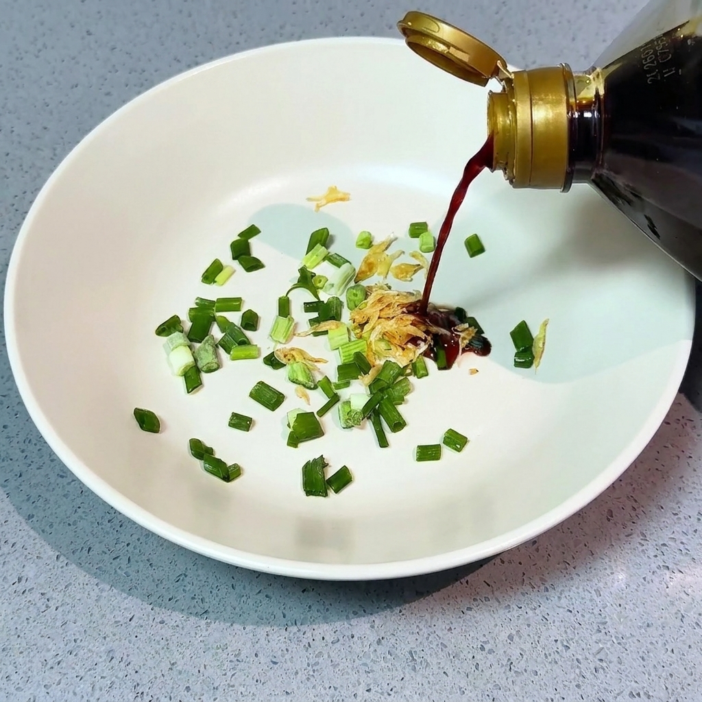 Helle Sojasauce wird aus einer Flasche über gehackte Frühlingszwiebeln und getrocknete Garnelen in einer weißen Schüssel gegossen.