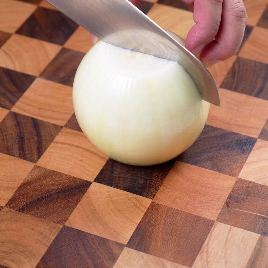 Gelbe Zwiebel wird auf einem Holzschneidebrett vorsichtig in dünne Streifen geschnitten.