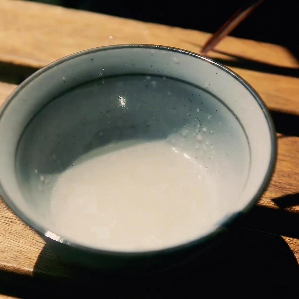 Eine kleine Keramikschale auf einer Holzoberfläche mit einer Mischung aus Sake, Zucker und Sojasauce.