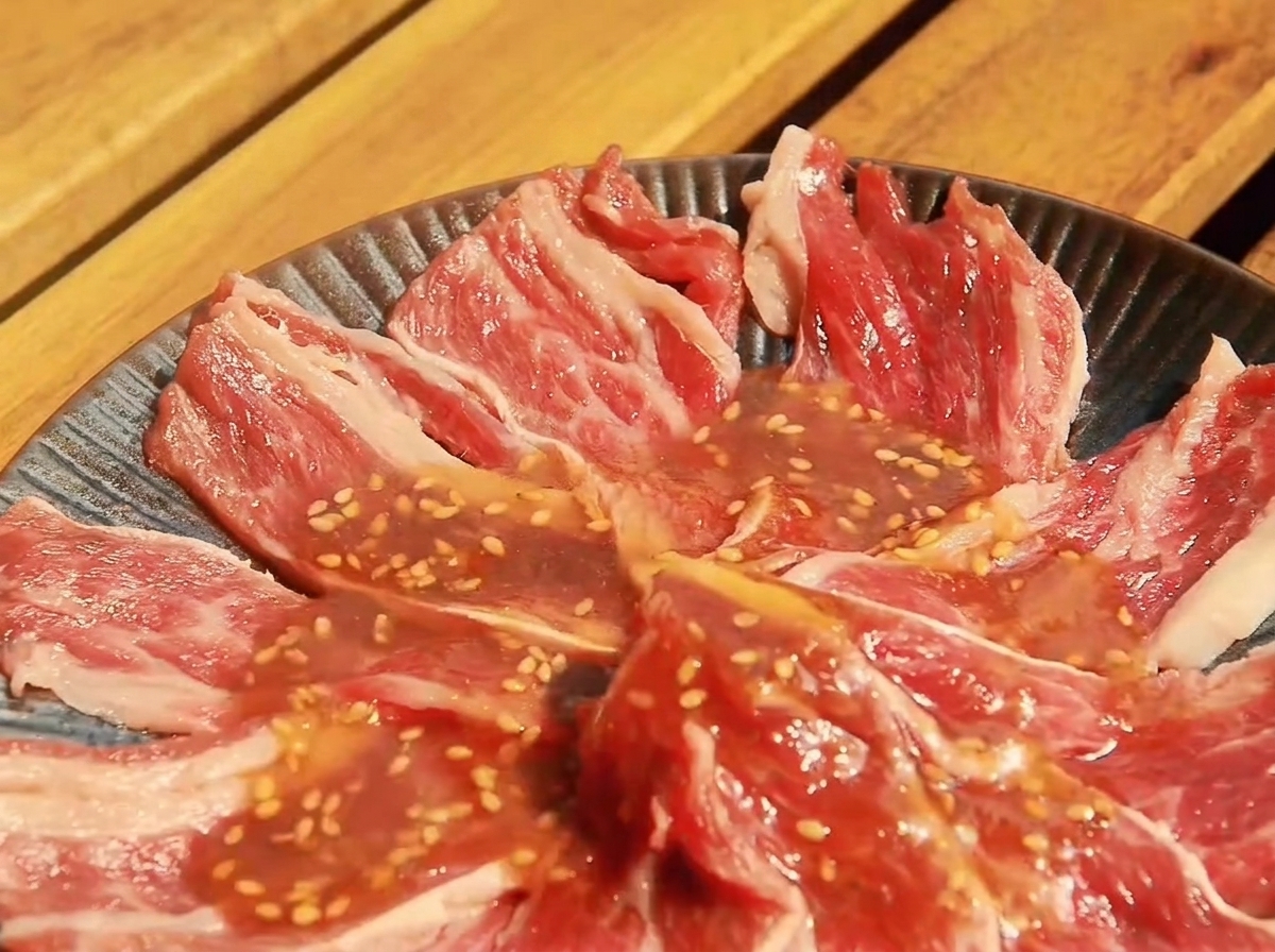 Dünne rohe Rindfleischscheiben in einer flachen Schale, bedeckt mit der vorbereiteten Yakiniku-Sauce.