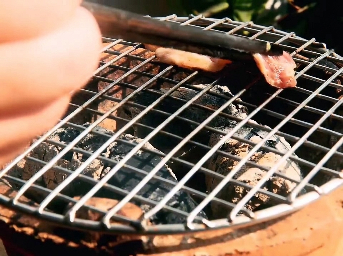 Marinierte Rindfleischstreifen auf einem heißen Grillrost, darunter glühende Kohlen.