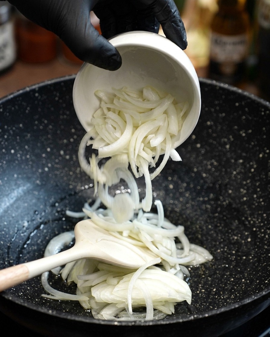 Frisch geschnittene weiße Zwiebeln werden in die Pfanne mit heißem Öl gegeben und umgerührt.