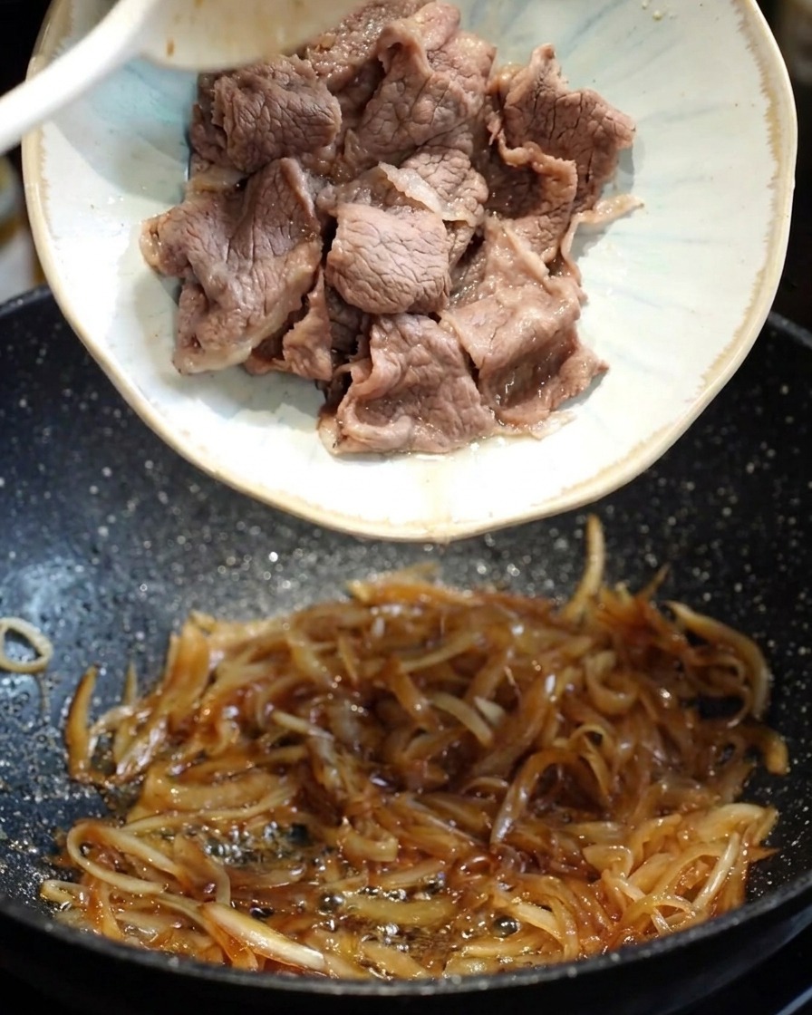 Eine dunkle, herzhafte Teriyaki-Sauce wird in die Pfanne mit Zwiebeln und Rindfleisch gegossen.