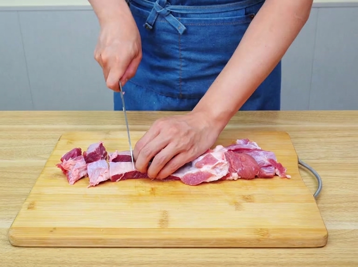 Rohes Rinderbrisket wird vorsichtig in große, gleichmäßige Stücke auf einem Holzbrett geschnitten.