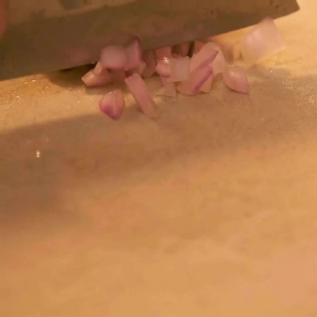 Eine Nahaufnahme eines scharfen Messers, das eine rote Zwiebel auf einem sauberen Schneidebrett fein würfelt.