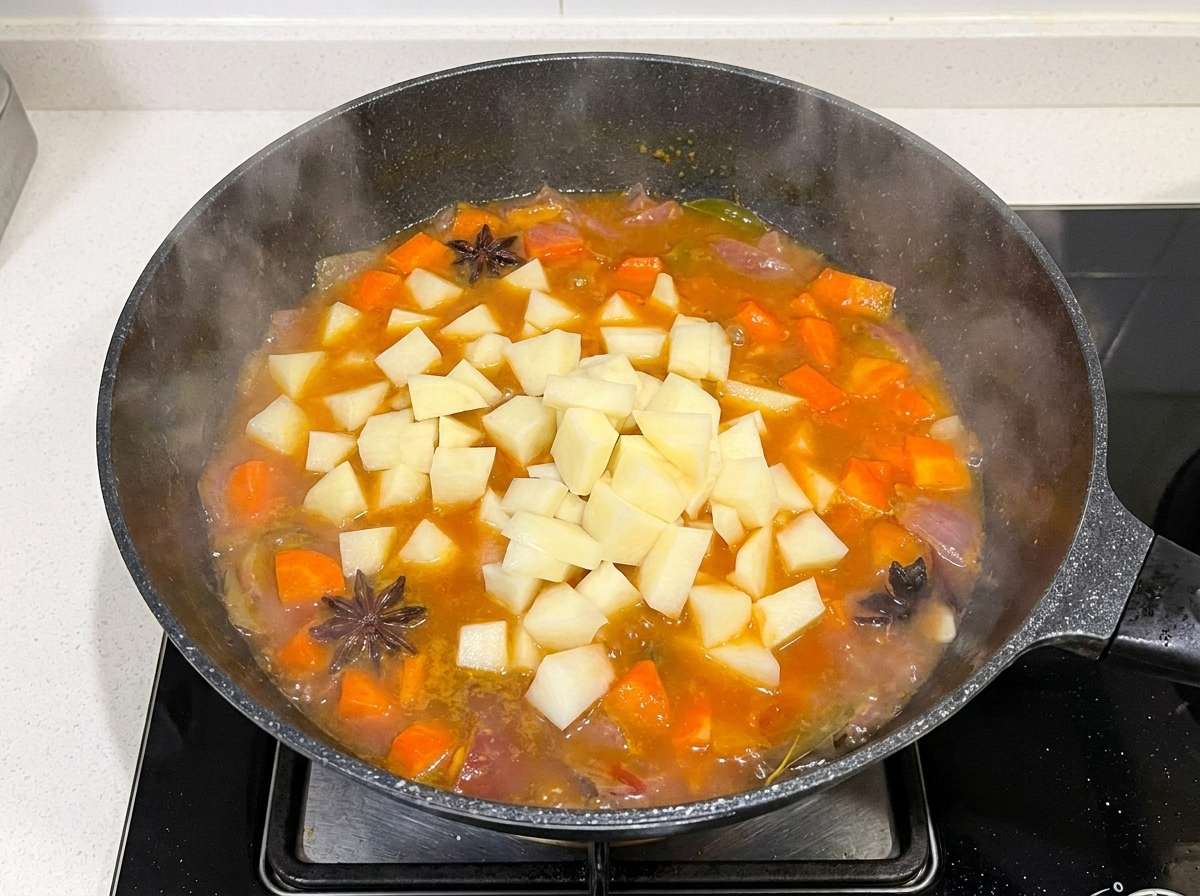 Gewürfelte Kartoffeln werden in eine Pfanne mit kochender Rinderbrühe, Karotten und Zwiebeln gegeben.