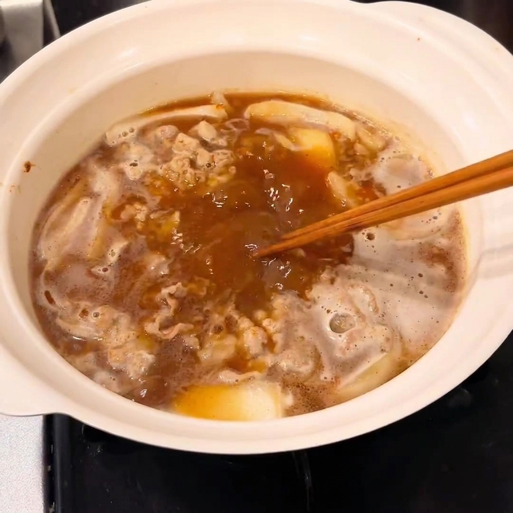 Ein Block Curry Roux wird in den Topf eingerührt, um eine angedickte Sauce zu bilden.