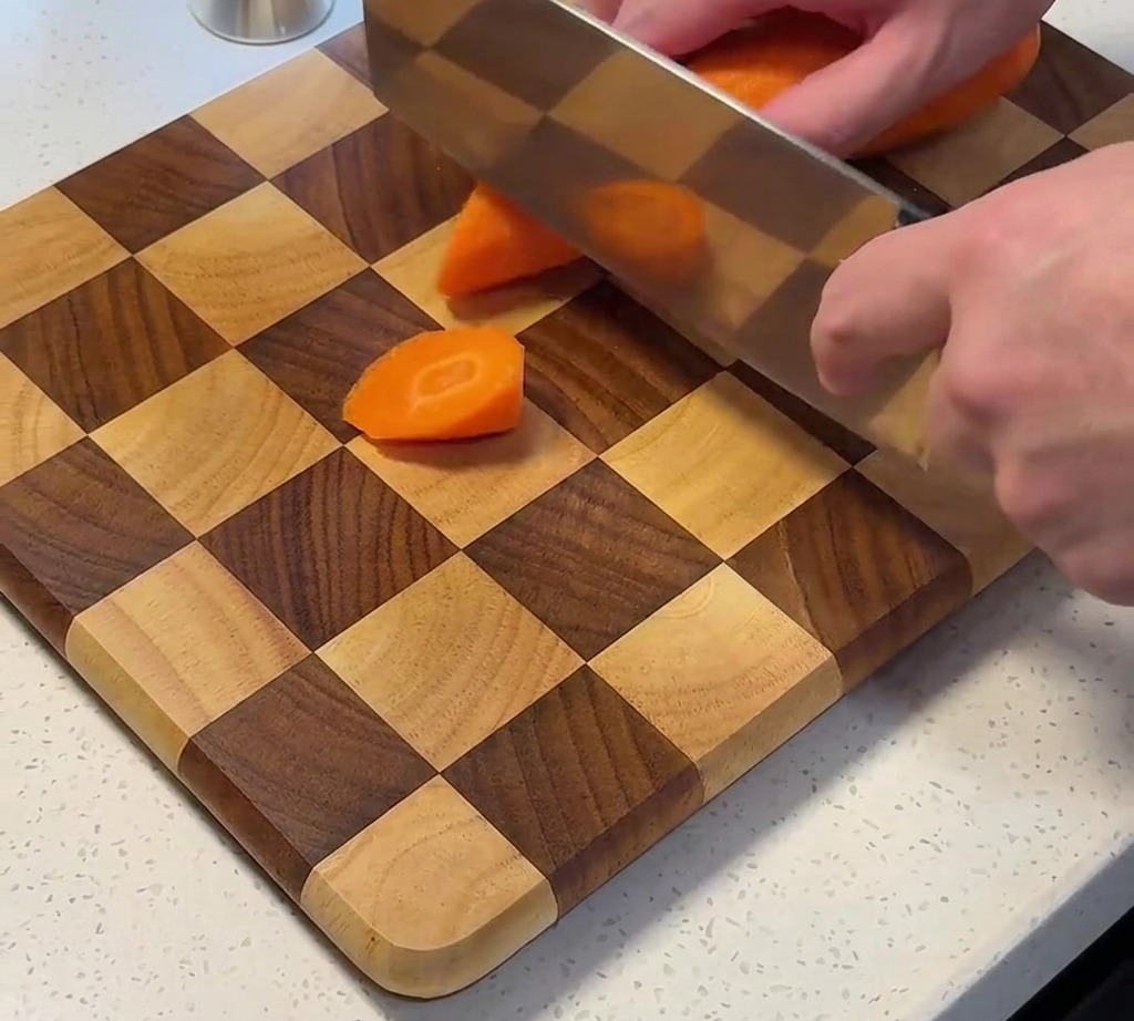 Frische Karotten werden auf einem Holzschneidebrett in Stücke geschnitten.