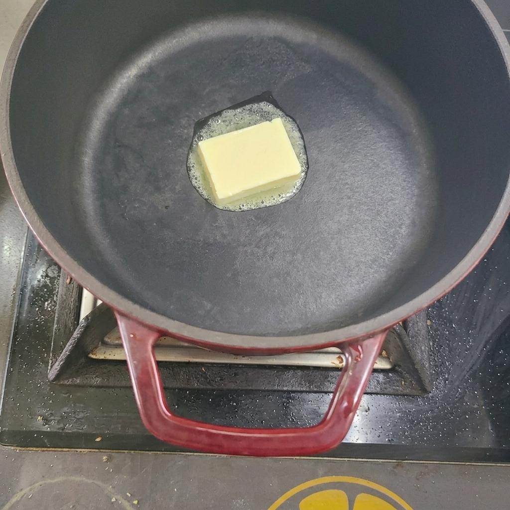 Ein Stück Butter schmilzt in einem schwarzen Topf auf dem Herd.