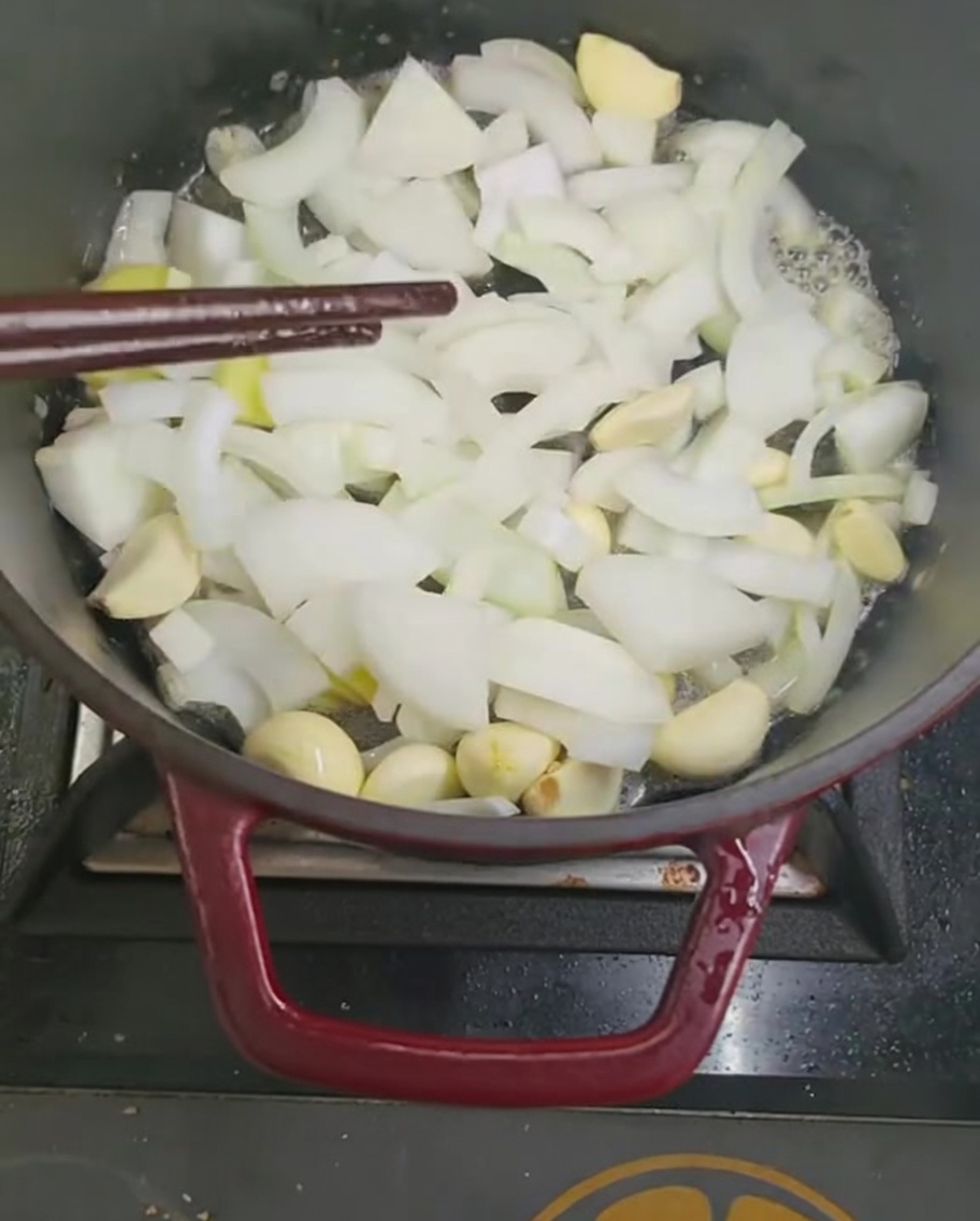 Zwiebel- und Knoblauchstücke werden in einem Topf mit Stäbchen angebraten.