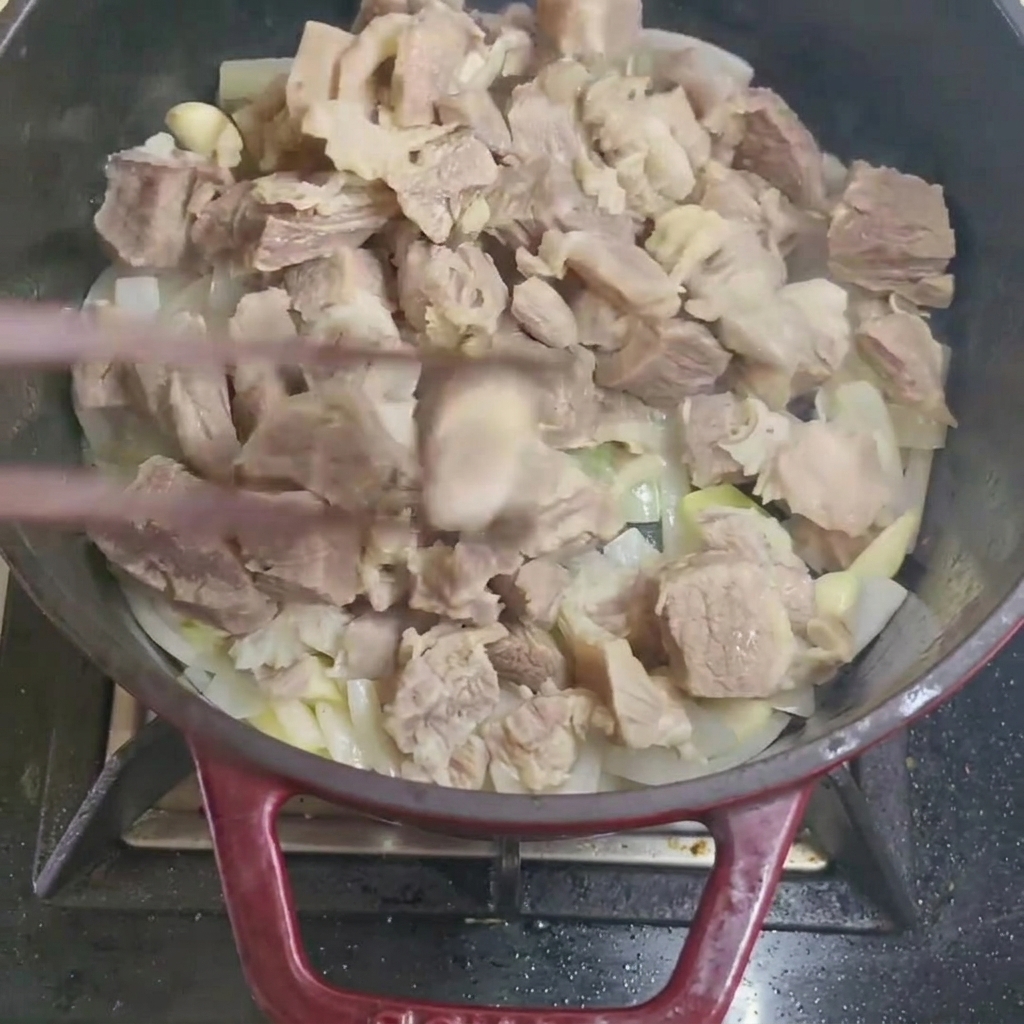 Blanchierte Rindfleischstücke werden mit Zwiebeln und Knoblauch in einer Pfanne vermengt.