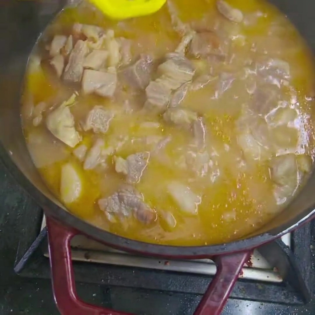Karotten- und Kartoffelstücke werden in den köchelnden Rindfleischeintopf im Topf gegeben.