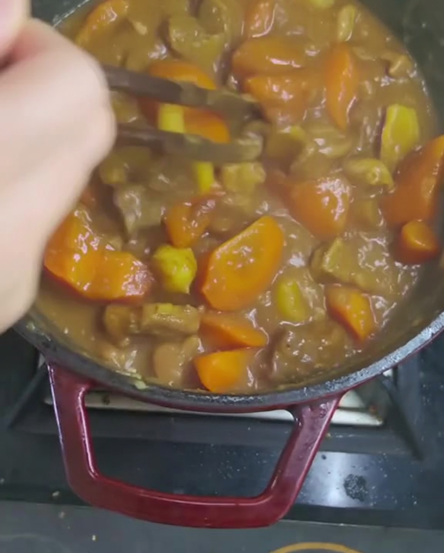 Die dicke Curry-Sauce wird mit einem Holzlöffel umgerührt, um die Curry-Würfel vollständig aufzulösen.