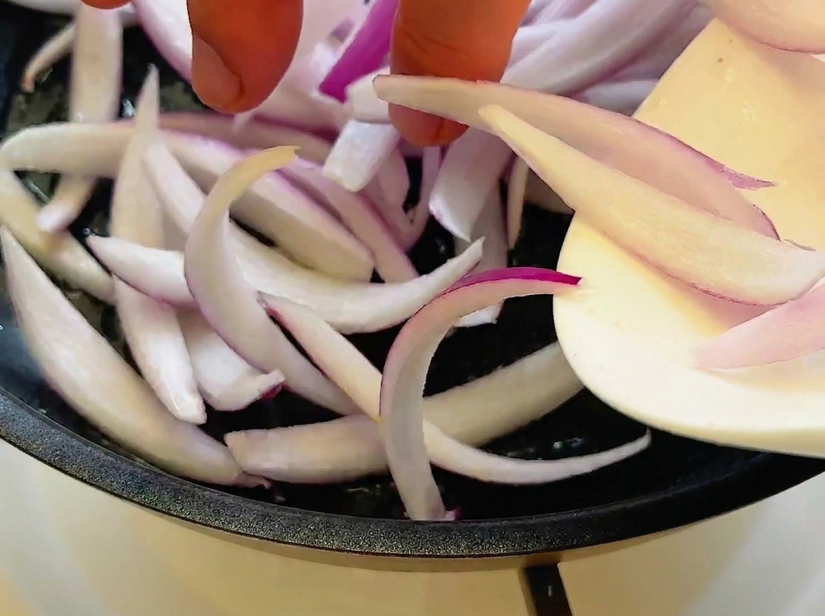 Rote Zwiebelscheiben werden in einer Pfanne glasig angebraten.