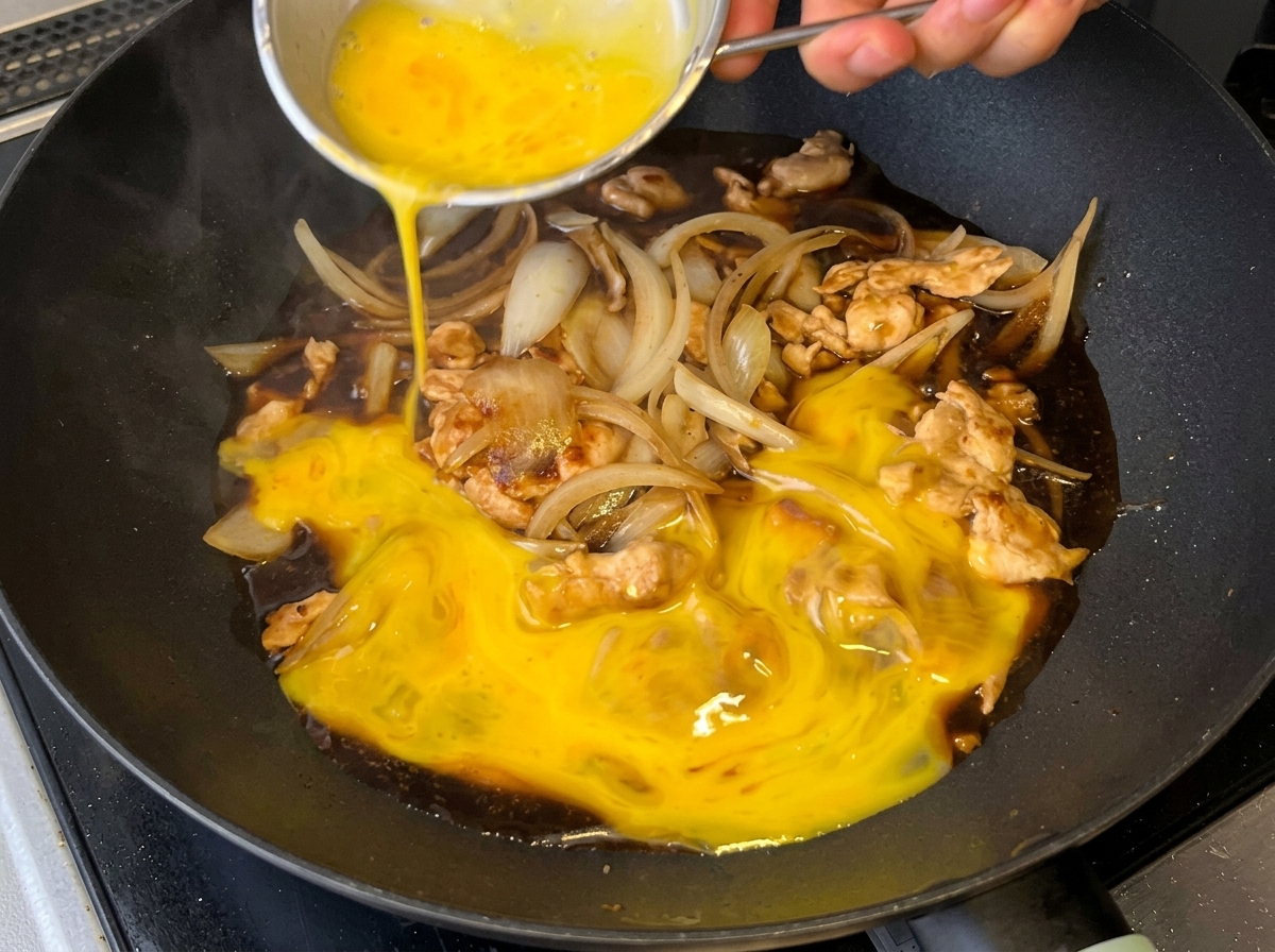 Verquirlte Eier werden über die Hähnchen-Zwiebel-Saucenmischung in der Pfanne gegossen.