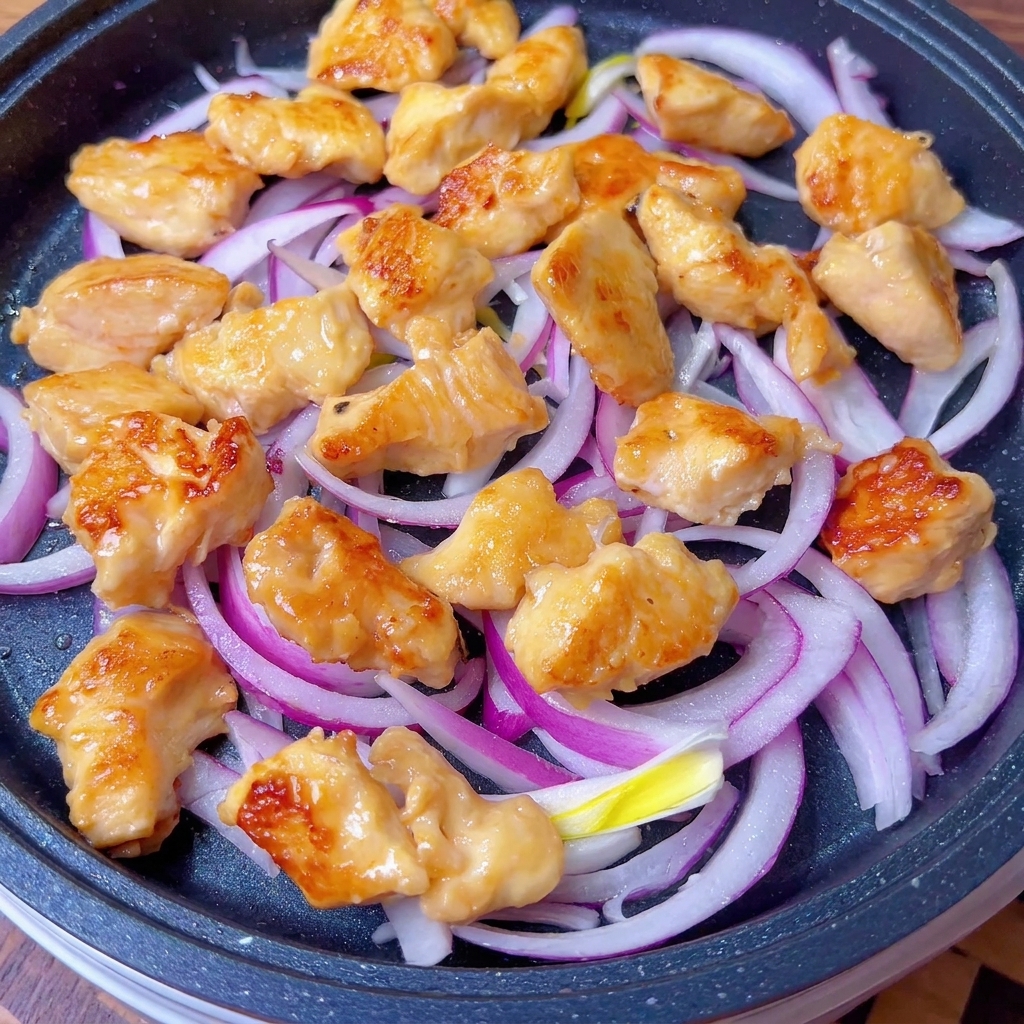 Goldbraune Hähnchenstücke und Zwiebeln werden in der Pfanne mit der herzhaften Sauce überzogen.