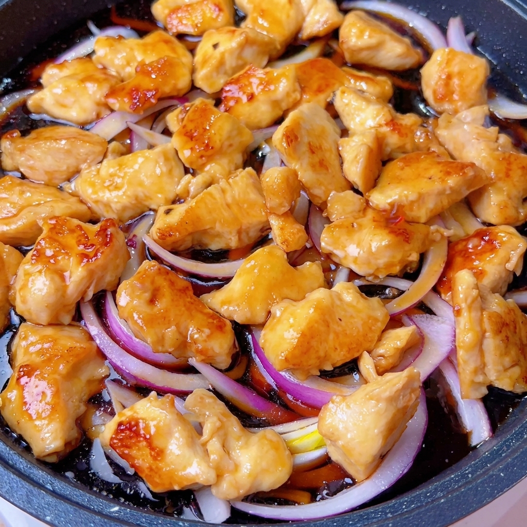 Eine abgedeckte Pfanne auf dem Herd, in der die Hähnchen-Zwiebel-Mischung köchelt.