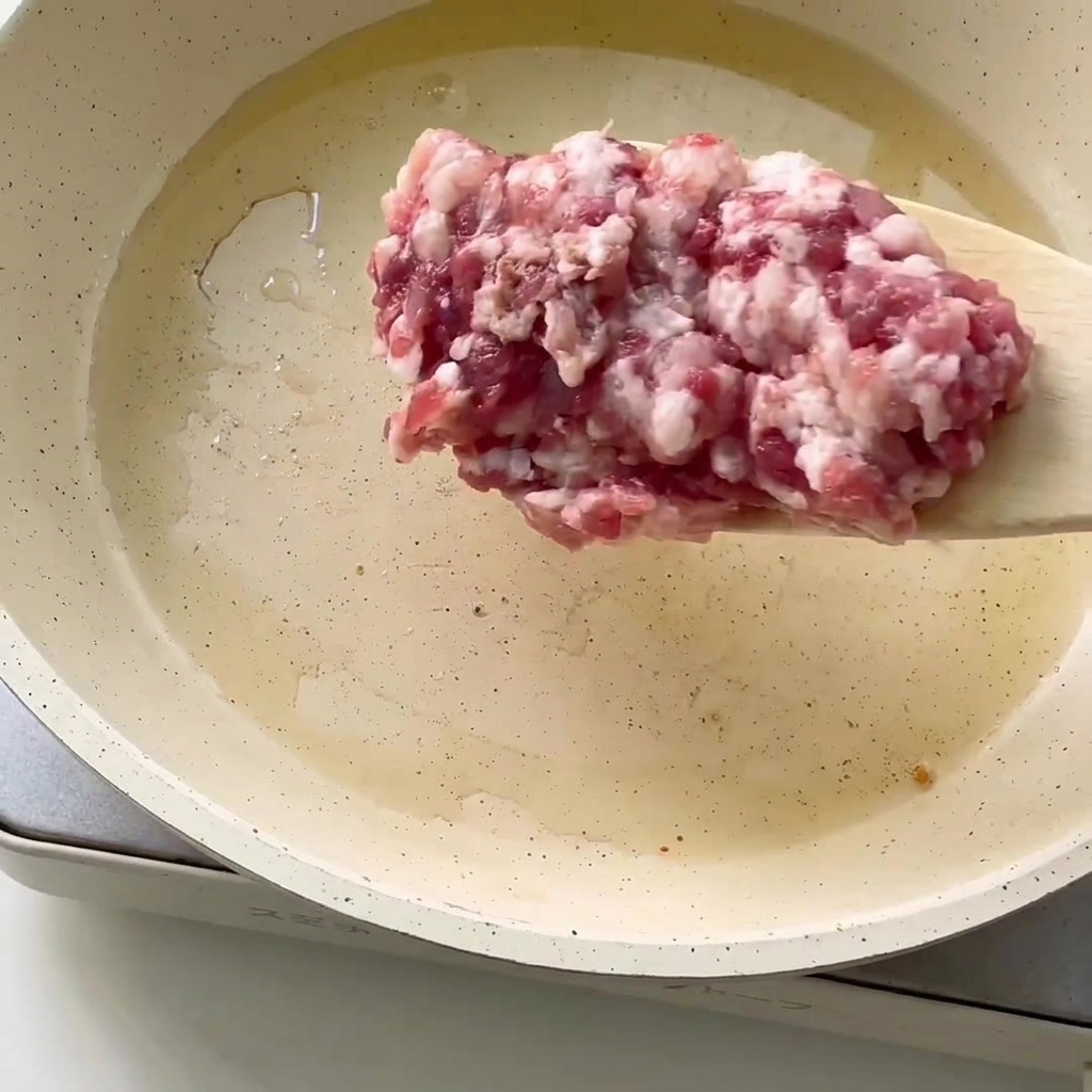 Nahaufnahme von frischem Hackfleisch in einer Pfanne mit heißem Öl.