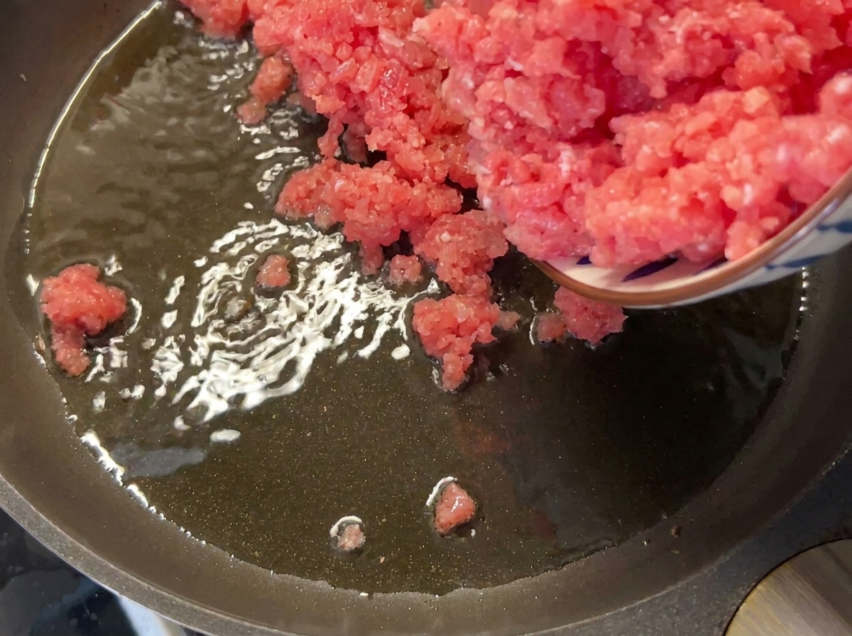 Mageres Schweinehackfleisch wird in eine heiße, geölte Pfanne gegeben.
