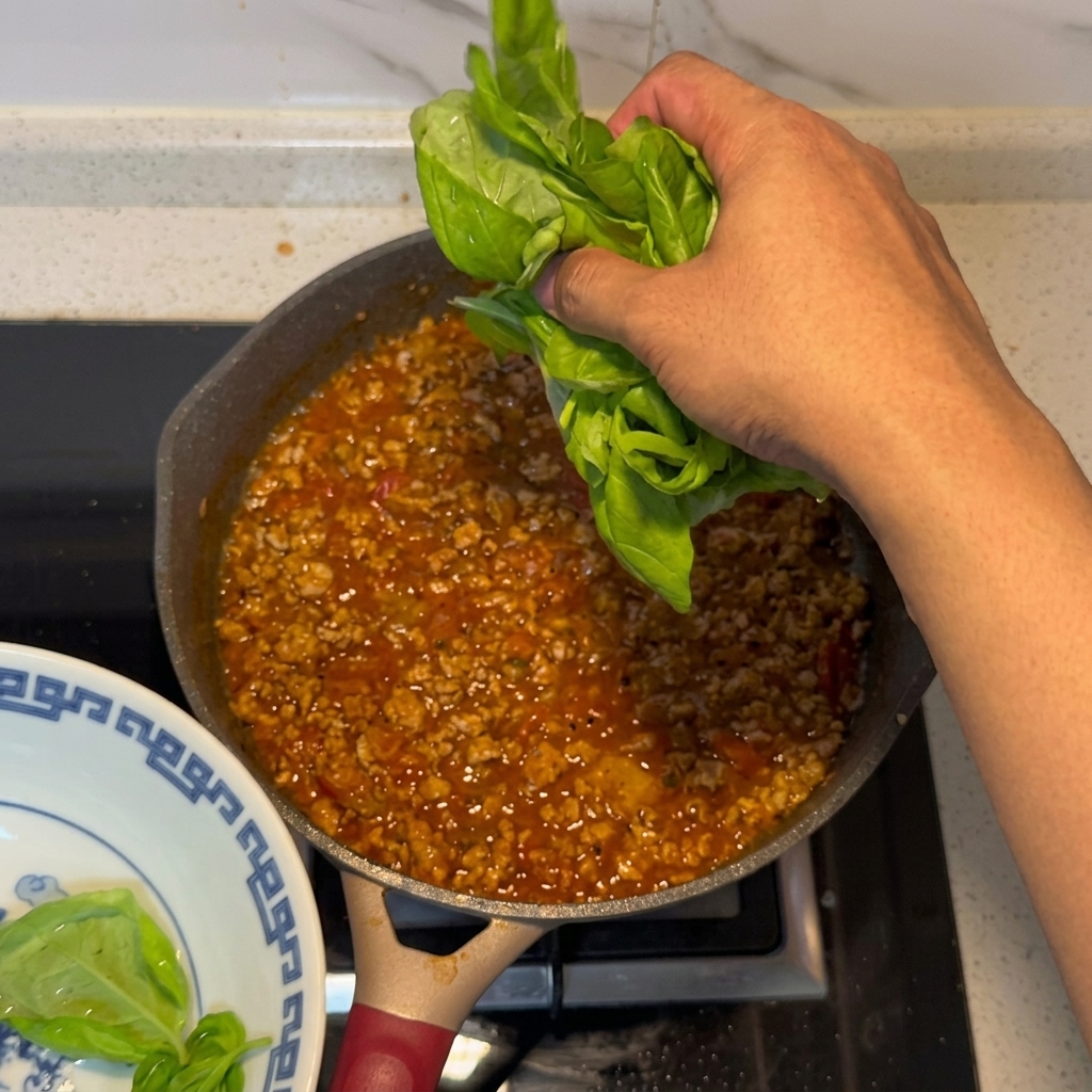 Frische Basilikumblätter werden unter die fertige Fleisch-Tomaten-Sauce gehoben.
